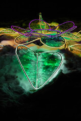 New Year street illumination in snow, a flower made of garlands. Snow as green smoke. Vertical template with space for copying. Festive multicolored lights on black background.
