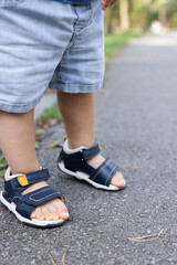 Little child has to clench his toes when he walks because wearing too small sandals.