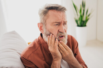 Photo of nice retired man sit couch touch cheek toothache wear brown clothes modern cozy interior...
