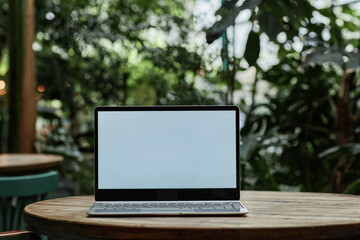 Silver laptop with white empty screen on wooden table in cafe