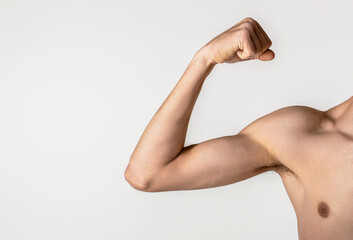 Young thin man arm on a grey background. Weak man muscle flexing. Skinny man goes in for sports, builds muscles. Man shows small biceps. Man is preparing for training. Sport and health concept