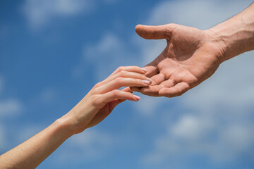 Hands of man and woman on blue sky background. Lending a helping hand. Solidarity, compassion, and...