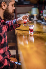 Hipster holds glass with alcoholic drink, short cocktail. Cocktails and bar concept. Bearded man shots cocktail. Tequila shots, vodka,whisky, rum. Man with cheerful sit at bar counter