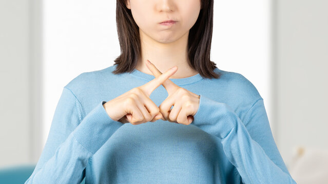 指でバツのポーズをする怒った表情の女性