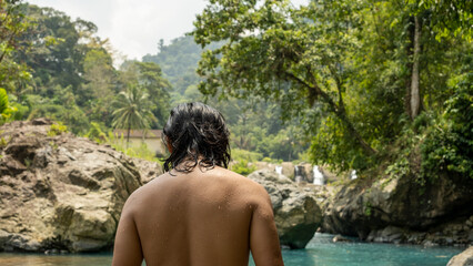 Fototapeta premium an Indonesian man, already swimming with a wet body with his back to the camera with a river background and extraordinary beautiful natural scenery