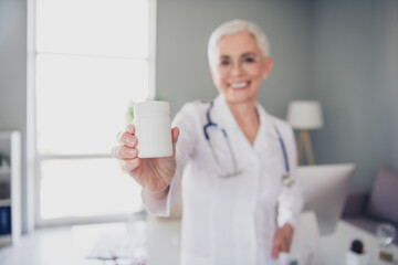 Portrait of aged woman professional doctor hold pills jar wear white coat workplace office indoors
