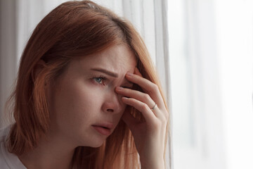 Portrait of a depressed woman: pale face, downcast eyes, expression of sadness and fatigue, shadows under the eyes, disheveled hair, blurred and dark