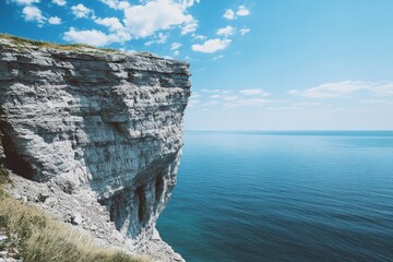 A majestic cliff extends over the vast, serene ocean under a bright blue sky with sparse clouds,...