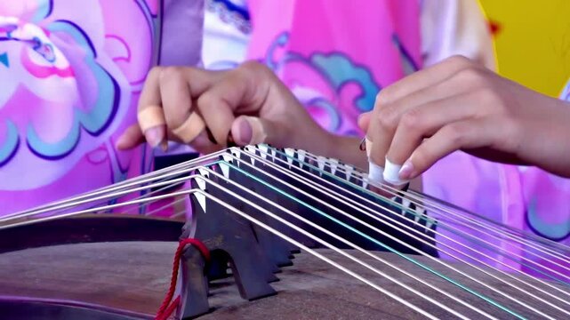 A person skillfully plucking the strings of a guzheng, a traditional Chinese zither. The musician's fingers, adorned with fingerpicks, glide effortlessly across the instrument.
