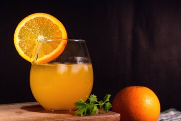 A glass of cold orange juice with a slice of orange on wooden table with dark background