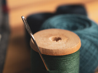 Close-up of a threaded needle and measuring tape against a background of fabrics, symbolizing the art of sewing and needlework