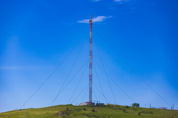 Red and white cellular base station with guy ropes is installed on top of a hill. Mobile...