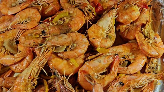 Pile of unpeeled grey shrimps cooked on hot steam and grilled with slices of onion, garlic cumin, slices of colored bell peppers and salt cooked and grilled, seafood cuisine of shrimps crustaceans