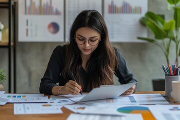 Focused young woman analyzing charts and data in a modern office setting with plants and reports around her