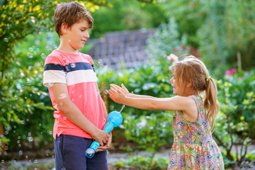 Happy little preschool girl and school kid boy having fun with blowing soap bubble blower....