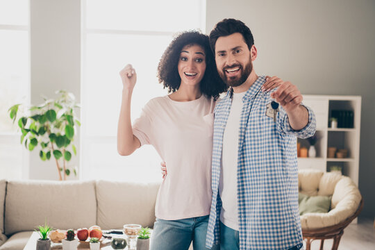 Photo of two nice young partners raise fist show key free time weekend modern apartment indoors