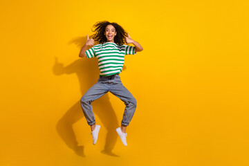 Full body portrait of nice young girl jump show thumb up wear striped t-shirt isolated on yellow color background