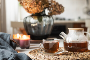 Warming autumn tea in glass cup, teapot and candles at modern kitchen. Home interior. Tea time, cozy atmosphere. Close up.