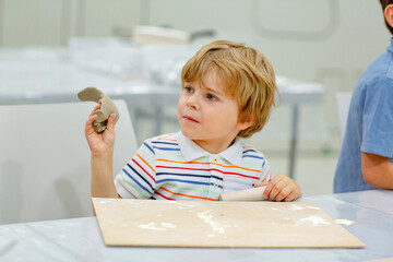 Little blond boy modeling with clay at master class art in a museum, indoors. Creative leisure for kids in kindergarden and at home, indoors.