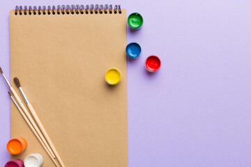 Album pages and paints, pencils, brush on a colored background. Top view with empty space. workplace for creativity. home teaching concept drawing