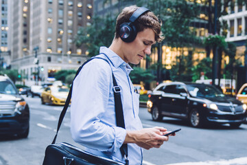 Side view of intelligent man checking received voice message via modern cellphone device listening via noise cancellation headphones, Caucasian male employee with briefcase search text on website