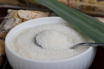 Granulated Sugar in White Bowl with Sugar Cane Stems and Leaf Decoration on Wooden Background