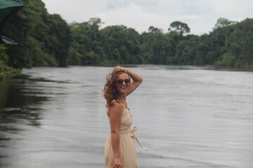 mulher com vestido claro e chapéu na beira de rio em hotel de selva em alta floresta, mato grosso 
