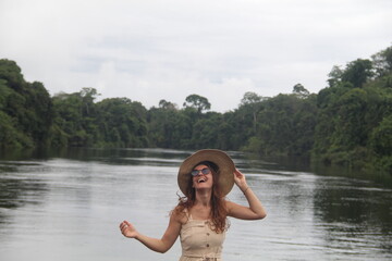 mulher com vestido claro e chapéu na beira de rio em hotel de selva em alta floresta, mato grosso 