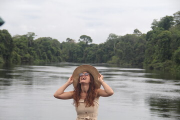 mulher com vestido claro e chapéu na beira de rio em hotel de selva em alta floresta, mato grosso 