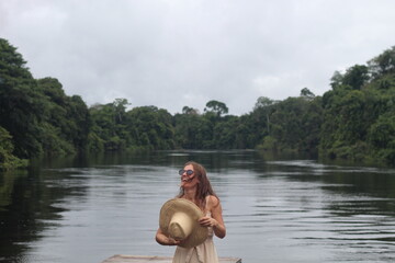 mulher com vestido claro e chapéu na beira de rio em hotel de selva em alta floresta, mato grosso 