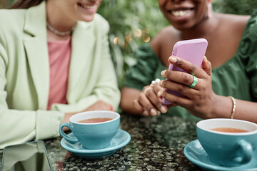 Medium closeup of pink smartphone in unrecognizable female hands, unrecognizable women scrolling social network together in cafe