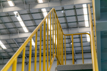 Industrial walkway with yellow handrail and steel structure roof inside the factory, equipped with a staircase secured by handrails.