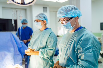Surgeons readying for surgery. Two surgeons in scrubs and masks focus intently as they prepare for...