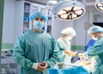 A man in a blue surgical mask stands in front of a surgical team. Scene is serious and focused, as...