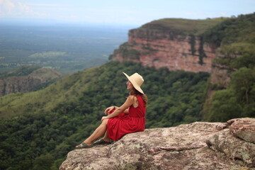 mulher de vestido vermelho e chapéu no mirante Alto do Céu, na Chapada dos Guimarães, Mato...