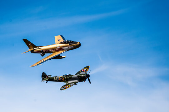 Two fighter planes commemorating different  wars:  (1) Korean War - F86 Sabre Jet (Decorated as a member of the RCAF Demonstration Team);  (2), W.W. II Spitfire, appearing at an Airshow..  