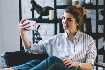 Positive millennial woman making selfie on modern mobile phone to upload in social networks, happy...