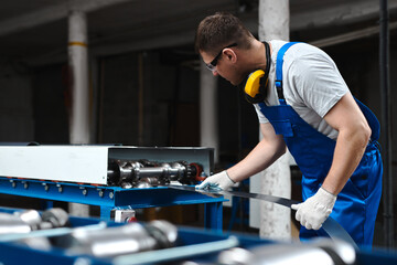Professional engineer man in blue uniform works in factory. Rolled metal, metal processing and manufacturing of metal fence