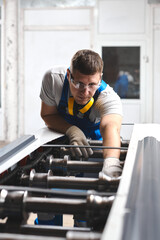 Professional engineer man in blue uniform works in factory. Rolled metal, metal processing and manufacturing of metal fence