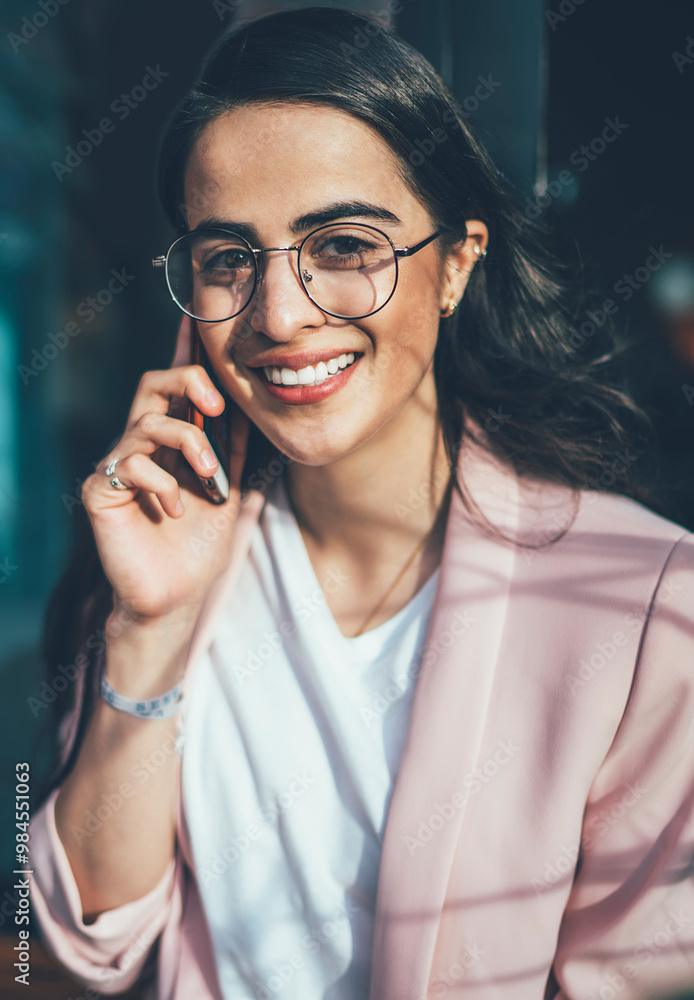 Poster portrait of smiling hipster girl in spectacles satisfied with tariffs for mobile calls in roaming ta