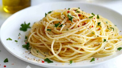 A plate of spaghetti aglio e olio with garlic and chili flakes, topped with parsley and olive oil, on a simple white background.