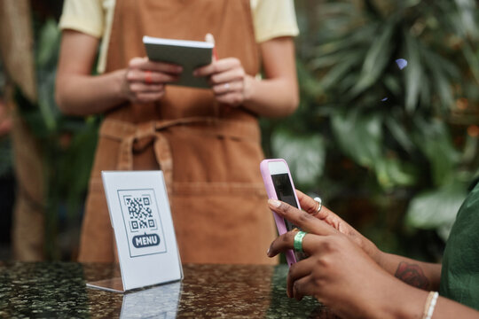 Side view shot of unrecognizable cafe visitor scanning qr-code to open online menu while unrecognizable waitress waiting for order