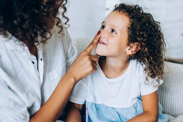 Playful woman touching nose of cute daughter