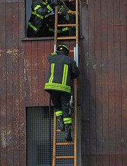 firefighter is climbing a wooden ladder during a training exercise at a fire station to enter a...