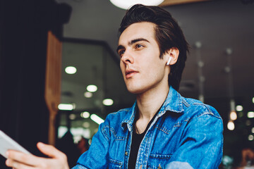 Thoughtful male student in bluetooth earphones pondering on information from psychological audio...