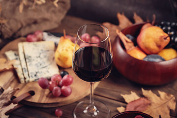 Glass of red wine served with blue cheese on dark wooden background. Autumn picnic with wine and cheese platter, fruits and dry leaves in rustic style
