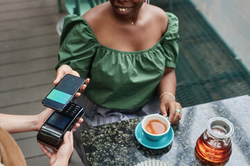 High angle shot of unrecognizable female hands holding smartphone and payment terminal