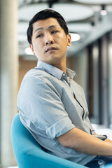 Asian man sitting in office chair, looking thoughtful and focused