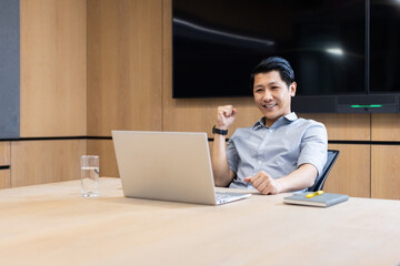 Celebrating success, asian man sitting at desk with laptop in modern office