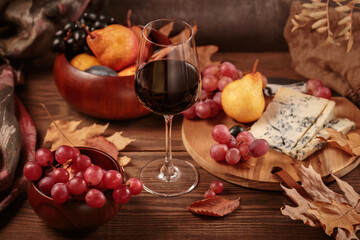 Glass of red wine served with blue cheese on dark wooden background. Autumn picnic with wine and cheese platter, fruits and dry leaves in rustic style